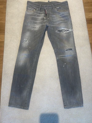 Dsquared2 Skater Jeans Grey - Säljer ett par äkta Dsquared2 Skater Jeans i grå tvätt med slitningar och färgstänk. Modellen är Skater Jean och storleken är 50 (S/M).  Jeansen är i mycket fint skick och har endast använts ett fåtal gånger. Knappt tvättade och väl omhändertagna. Inga skador eller fläckar utöver den design som är original från Dsquared2.  ✔️ 100 % äkta Dsquared2 ✔️ Kvitto finns ✔️ Modell: Skater Jean ✔️ Storlek: 50 (ca M) ✔️ Färg: Grey Wash / Grå tvätt ✔️ Tillverkade i Italien ✔️ Mycket fint skick