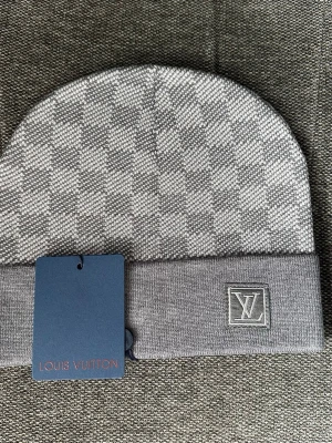 Grå mössa med rutmönster - Snygg grå mössa med klassiskt rutmönster och vikt kant. Logga broderad framtill på kanten. Tillverkad i mjukt stickat material som känns lyxigt och stilrent. Perfekt accessoar för att lyfta din outfit.