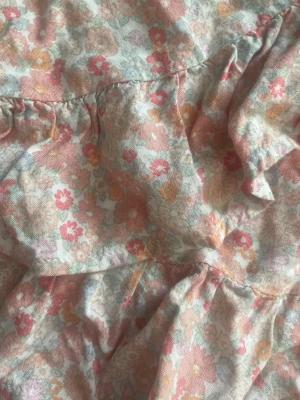 Blommig omlottkjol med volang - Supersöt kort omlottkjol med volangkant och blommigt mönster i ljusa pastellfärger som rosa, orange och beige. Kjolen har knytband i midjan och är perfekt för vår och sommar. Materialet känns lätt och luftigt. Andvändes för några år sedan så finns antagligen inte att köpa längre. Den har två små hål som knappt syns och som jag inte märkt innan. Storlek 146/152 men jag som 170 kan andvända den som en tajt kjol. Annars är den luftig. Från Kappahl, hör av er vid frågor!