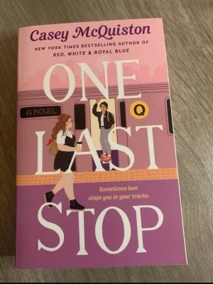 One Last Stop av Casey McQuiston - En färgstark pocketbok med lila och rosa omslag, illustrerad med två personer vid en tunnelbana. Titeln 'One Last Stop' och författaren Casey McQuiston syns tydligt. Perfekt för dig som gillar romantisk och modern skönlitteratur.