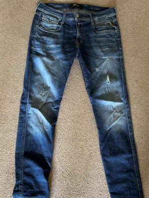 Replay Anbass - Säljer ett par blå jeans ifrån Replay skinny fit och slitningar på låret. Jeansen har klassisk femficksdesign, ljusa tvättade partier och kontrastsömmar. Materialet är denim i bomull. Perfekta för en avslappnad och trendig look.