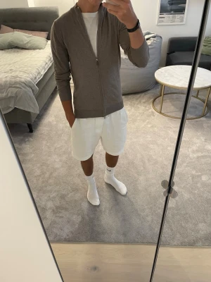 Stenströms merinozip  - Säljer en stilren beige ziptröja med hög krage och långa ärmar. Tröjan har en smal passform och är tillverkad med merinoull. Perfekt att slänga över en t-shirt för en clean och enkel look.