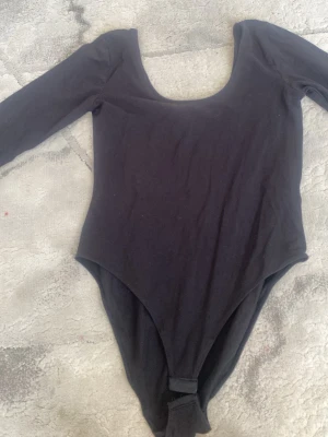 Svart långärmad body - En enkel och stilren svart body med långa ärmar och rundad urringning. Tillverkad i mjukt stretchigt material som sitter skönt mot kroppen. Perfekt att matcha med jeans eller kjol för en clean look.