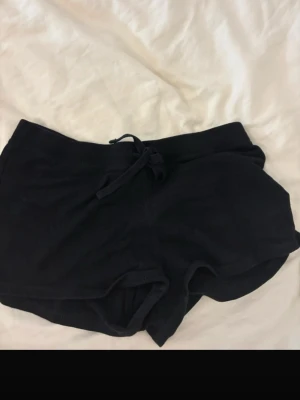 Svarta shorts med snörning från H&M - Ett par svarta shorts från H&M i mjukt material med snörning i midjan. De har en enkel och avslappnad design, perfekt för chill dagar eller träning. Shortsen har en loose passform och är midwaist.