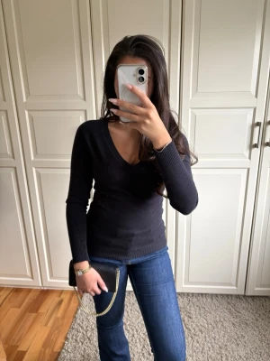 Svart stickad v-ringad tröja - Klassisk svart stickad tröja med v-ringning och långa ärmar. Tröjan har en smickrande passform och ribbade muddar vid ärmslut och nederkant. Perfekt att matcha med jeans eller kjol för en enkel och stilren look.