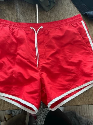 Två par retro badbyxor i rött och blått - Säljer två par snygga badbyxor i retrostil, ett par röda och ett par blå. Båda har vita detaljer längs kanterna och vita dragsnören i midjan. Perfekta för stranden eller poolen och har en klassisk, sportig look.