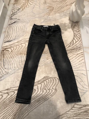 Svarta jeans från Zara för barn - Säljer ett par svarta  jeans från Zara i storlek 134 för barn. Jeansen har klassisk femficksdesign, normal midja och smal passform hela vägen ner. Snygg tvätt med lätt slitning för en trendig look. Perfekta till vardagsoutfiten!