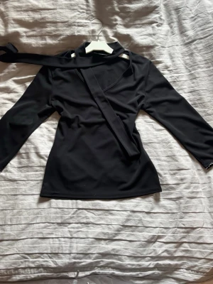 Svart långärmad topp med strassdetalj - Snygg svart långärmad topp med knytning i halsen och strassdetaljer längs ärmen. Toppen är figursydd. Från Kappahl, köpt second hand men fortfarande i bra skick