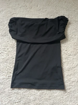 Svart off shoulder topp - Trendig svart off shoulder topp med puffiga ärmar och åtsittande passform. Tillverkad i mjukt och stretchigt material som ger en snygg siluett. Perfekt för dig som vill ha en stilren och modern look. Aldrig använd😍