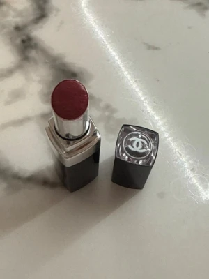 Chanel mörkrött läppstift - Snyggt mörkrött läppstift från Chanel med elegant svart och silverhylsa. Locket har den klassiska Chanel-loggan i vitt. Läppstiftet har en krämig formula och ger en djup, intensiv färg till läpparna.
