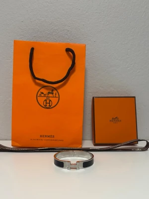 H armband svart silver  - Stilrent H armband i emalj och silverfärgad metall. Armbandet har den ikoniska H-detaljen framtill och en elegant, rund form. Perfekt accessoar för att lyfta din outfit med en lyxig touch. Hör av dig vid minsta intresse! 🤝