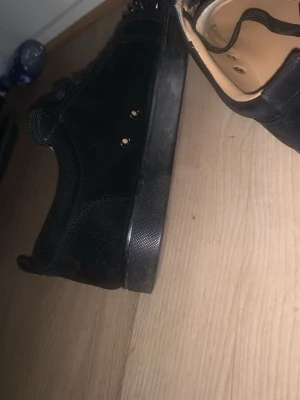 Svarta sneakers med nitar - Säljer ett par svarta Loubs med coola svarta nitar på tån och hälen. Skorna är A-Kopior och de har svart mockaliknande material, svarta skosnören och röd sula med text. Insidan är beige och de har en klassisk låg profil. Priset kan absolut diskuteras.