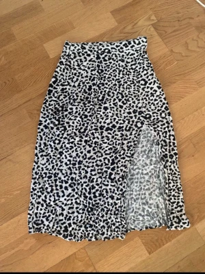 Leopardmönstrad kjol från Amisu - Säljer en snygg leopardmönstrad kjol från Amisu i storlek 34. Kjolen är vit och svart med en hög midja och en slits på sidan som ger en trendig look. Perfekt för dig som vill sticka ut lite extra.