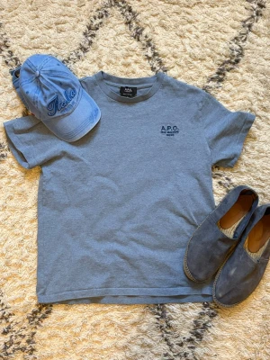 Ljusblå t-shirt från A.P.C. - Snygg ljusblå t-shirt från A.P.C. med diskret logga på bröstet. Klassisk passform och rund halsringning. Tillverkad i mjuk bomull, perfekt för en clean och stilren look. Storlek M! (Espandrillos och keps kommer ej med)