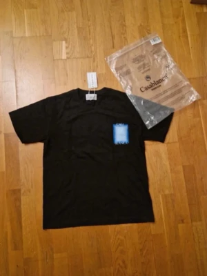 Svart t-shirt från Casablanca - Svart t-shirt från Casablanca med klassisk passform och korta ärmar. T-shirten har en liten blå detalj på bröstet och är tillverkad i mjuk bomull. Perfekt för en clean och stilren look.