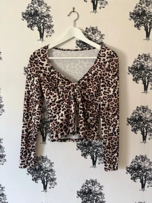 Leopardmönstrad långärmad topp - Snygg långärmad topp med leopardmönster och v-ringning. Toppen har en croppad passform och knytning framtill som ger en trendig look. Perfekt för dig som vill sticka ut med ett djurmönster. Mjuk och stretchig känsla.