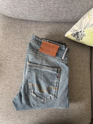 Blå jeans från Replay - Säljer ett par klassiska blå jeans från Replay i modellen Willbi. Jeansen har en snygg tvätt, fem fickor och detaljerade sömmar på bakfickan. Tillverkade i slitstarkt denim med läderpatch bak i midjan. Perfekta för en avslappnad och trendig look.