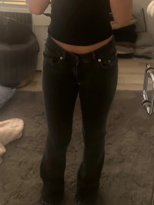 Svarta bootcut jeans med låg midja - Säljer ett par svarta bootcut jeans med låg midja och klassisk femficksdesign. Jeansen har en snygg passform som sitter tajt över låren och släpper ut vid bensluten. Perfekta till en trendig vardagslook.