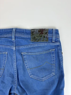 Blå slim fit jeans från Jacob Cohen - Snygga blå jeans från Jacob Cohen i slim fit-modell med klassiska fem fickor och detaljerade sömmar. Jeansen har en patch med logga baktill i midjan och är tillverkade i mjuk denim med stretch för extra komfort.