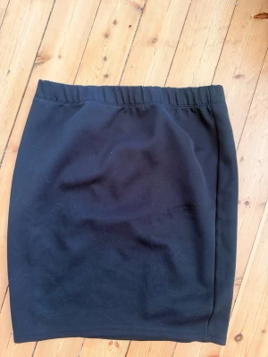 Svart enkel kortkjol - En stilren svart kortkjol med rak passform och resår i midjan. Kjolen är enkel och lättmatchad, perfekt till många olika looks. Materialet känns mjukt och bekvämt mot huden.