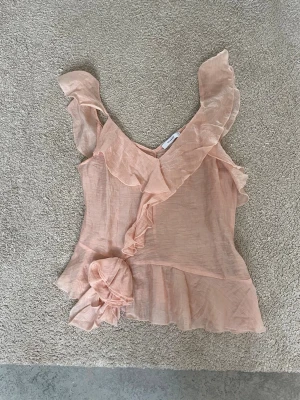 Ljusrosa volangtopp från Reserved - Supersöt ljusrosa topp från Reserved med volangdetaljer och stor rosett framtill. Jättefin till sommaren och jättebra passform. Toppen är inte stretchig och säljs billigare pga små defekter, däremot har det inte varit några större problem för mig och skulle säga att de knappast syns!💞