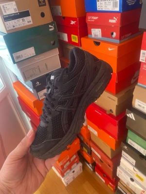 Svarta Asics Gel-1000 sneakers - Säljer ett par helsvarta Asics Gel-1000 sneakers med mesh- och syntetmaterial. Skorna har en chunky sula och klassisk Asics-logga på sidan. Perfekta för dig som gillar sportig och stilren look. Skön dämpning och snygg design.