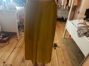 Gul plisserad midikjol - Säljer en snygg gul plisserad midikjol med hög midja. Kjolen har ett flowy fall och är perfekt för dig som vill sticka ut med färg. Passar till både sneakers och klackar för en trendig look.