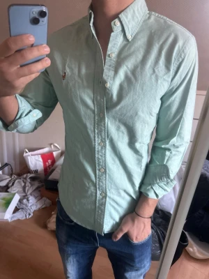 Ljus skjorta från Ralph Lauren - Snygg skjorta från Ralph Lauren med klassisk button-down krage och broderad logga på bröstet. Skjortan har långa ärmar och vita knappar framtill. Perfekt för en stilren och avslappnad look.