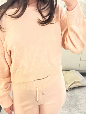Beigeset loungewear-set i mjuk trikå - Säljer ett supermysigt loungewear-set i beige mjuk trikå. Setet består av en långärmad tröja med bred mudd och matchande byxor med dragsko i midjan och bakficka. Perfekt för chill dagar hemma eller när du vill vara bekväm men ändå snygg. Lite smutsiga längst ner
