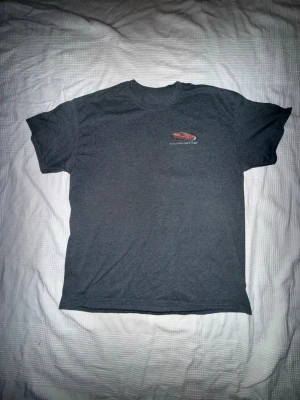 Corvette T-shirt - Snygg mörkgrå T-shirt med stilrent Corvette-tema. Liten logga framtill och större tryck på ryggen med en röd Corvette samt flera klassiska modeller och texten “Living Legend”. Perfekt för bilentusiasten eller som en cool vardagströja.