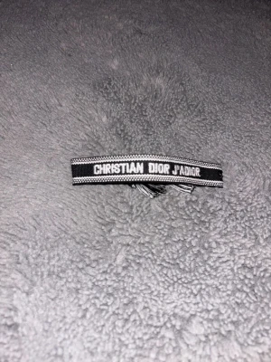 Christian Dior J'Adior armband svart - Snyggt svart och vitt armband från Christian Dior med texten 'J'Adior'. Armbandet är vävt i tyg och har justerbara band för perfekt passform. Perfekt accessoar för dig som vill ha en exklusiv och trendig look. Pris kan diskuteras!!! 