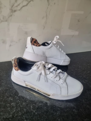 Vita sneakers Tommy Hilfiger leo-detalj - Snygga vita sneakers från Tommy Hilfiger med leopardmönstrad detalj vid hälen och guldfärgad rand på sulan. 
