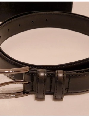 Svart skärp 42" XL med silverfärgat spänne - Stilrent svart skärp med klassiskt silverfärgat spänne. Skärpet har släta kanter och flera hål för justering. Perfekt för att lyfta din outfit med en enkel och snygg detalj.Svart skärp 42" XL med silverfärgat spänne