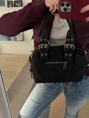 Svart handväska med nitar och dragkedja - Cool svart handväska med dubbla handtag, silverfärgade nitar och detaljer samt dragkedja framtill. Från Núnoo 🩷  Super snygg och går att bära i handen och över axeln då remmar ingår 🥰 Pris kan diskuteras! — 33x19 cm