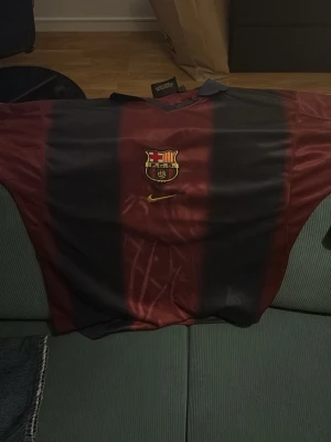 Barça x Cactus Jack fotbollströja - Säljer en unik Barcelona fotbollströja i samarbete med Cactus Jack. Tröjan har klassiska blå och vinröda ränder, klubbemblem på bröstet och Nike-logga. På ryggen står det 'Cactus Jack', nummer 2 och 'BARÇA' i orange. Perfekt för dig som vill sticka ut på planen.