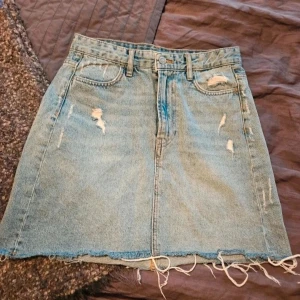 Jeanskjol H&M 36 - Säljer en ljusblå jeanskjol i klassisk femficksmodell med slitna detaljer och rå, fransig fåll. Kjolen har bälteshällor, dragkedja och knapp framtill samt slitningar både fram och bak för en cool, avslappnad look.  Kan även hämtas I Partille  E2