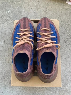 Yeezy Boost 380 bruna/blå sneakers - Unika Yeezy Boost 380 sneakers i brunt och blått med beige snörning. Ovandelen är i stickad mesh som ger en skön och flexibel passform. Sulan är tjock och ger bra dämpning, perfekt för dig som gillar streetwear och vill sticka ut.