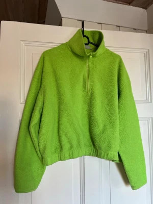 Limegrön stickad fleece-tröja - Limegrön stickad tröja i fleece med hög krage och halv dragkedja framtill. Tröjan har avslappnad passform, långa ärmar och resår i midjan. Perfekt för lager-på-lager och när du vill sticka ut med färg.