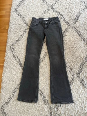 Svarta bootcut jeans från Junkyard  - Snygga grå/svarta bootcut jeans från Junkyard med klassisk femficksdesign och lägre midja. Jeansen har en lätt tvättad look och är tillverkade i stretchigt denim för skön passform. Perfekta för dig som gillar en trendig siluett. Slitna längst ner se bild 5.