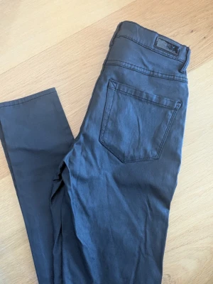 Svarta skinny jeans från ONLY - Säljer ett par svarta skinn/ läder skinny jeans från ONLY med klassisk femficksdesign och snyggt läderpatch bak. Jeansen har smal passform och är tillverkade i ett stretchigt material som sitter bekvämt. Perfekta för dig som gillar en stilren look.