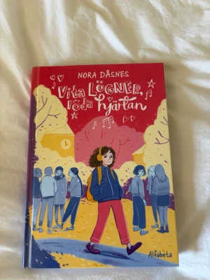 Vita lögner, röda hjärtan - En färgglad grafisk roman av Nora Dåsnes med hårda pärmar. Boken handlar om vänskap, kärlek och att hitta sig själv i tonåren. Omslaget har illustrationer i rött, gult, blått och lila med en tjej i centrum och skolmiljö i bakgrunden.