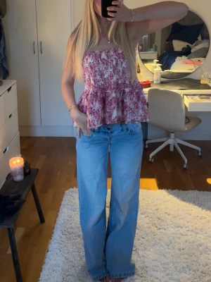 Blommig volang i rosa och vit - Kjol även. Supersöt blommig topp i rosa och vitt med volang och luftig passform. Toppen är ärmlös och har en avslappnad, flowy stil som passar perfekt till jeans eller kjol. Perfekt för varma dagar och ger en romantisk vibe.