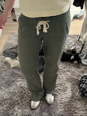 Gröna linnebyxor  - Snygga Roxy gröna linnebyxor med avslappnad passform och vit dragsko i midjan. Byxorna har raka ben och två fickor framtill. Perfekta för en chill och bekväm stil.