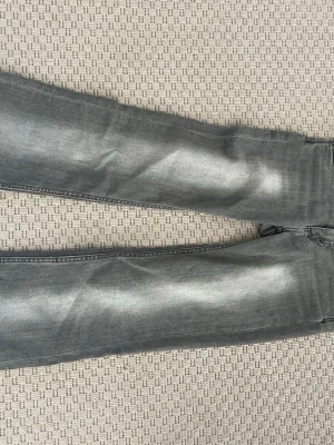 Grå raka jeans med tvättad look - Säljer ett par grå bootcut jeans och snyggt tvättad effekt på benen. Jeansen har klassisk femficksdesign och är tillverkade i denim. Perfekta för dig som gillar en avslappnad och trendig stil. Lite uppsydda