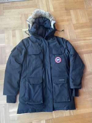 Svart parkas från Canada Goose - Snygg svart parkasjacka från Canada Goose med klassisk patch på bröstet. Jackan har fyra stora fickor framtill, varm huva med päls och justerbar dragsko. Perfekt för kalla vinterdagar och riktigt streetig stil. Nypris ca 15000. Storlek S/P. Passar dig som är ca 172-185. Vid intresse kan man få mått! Den är begagnad så titta noga på bilderna innan du köper! Mvh Oliver 