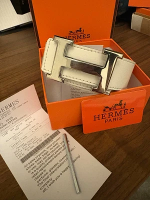 Vitt h bälte - Exklusivt vitt skärp från H med stor, ikonisk H-spänne i silverfärgad metall. Skärpet är tillverkat i skinn och levereras i originalförpackning med tillhörande certifikat och kvitto. Perfekt accessoar för att lyfta din outfit.