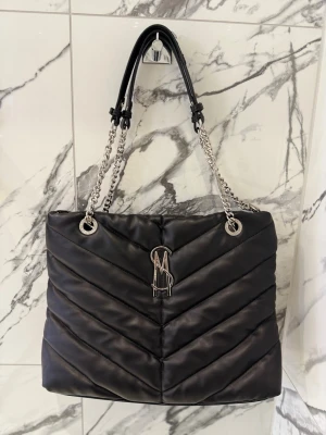Svart handväska - Steve Madden - Snygg svart quiltad handväska från Steve Madden med silverfärgade kedjehandtag och logotyp framtill. Inga skador eller defekter 