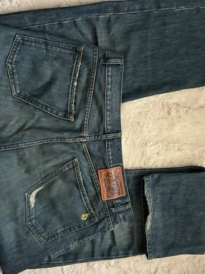 Blåa jeans från Volcom 33x32 - Snygga blå jeans från Volcom med klassisk femficksdesign och läderpatch bak. Jeansen har raka ben och subtila slitningar vid bakfickorna. Tillverkade i bomullsdenim med en cool tvättad look.