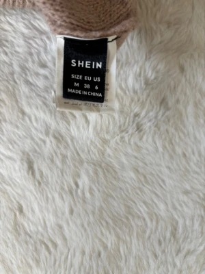 Beige kabelstickad tröja från SHEIN - Säljer en beige kabelstickad tröja från SHEIN i storlek M. Tröjan har breda ribbade muddar vid ärmslut och nederkant, samt ett snyggt kabelmönster framtill. Materialet är mjukt och tröjan har en avslappnad passform med ballongärmar. Använd några få gånger, pris kan diskuteras. 