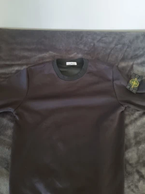 Svart sweatshirt från Stone Island - Cool svart sweatshirt från Stone Island med klassisk rund hals och ribbade muddar. Ikonisk logotyp-patch på vänster ärm. Perfekt för en stilren och avslappnad look.